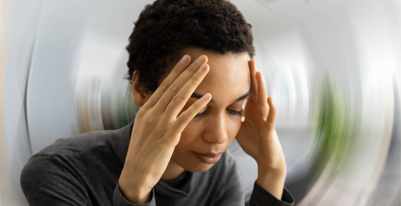 Woman experiencing dizziness and vertigo, holding her head, with a blurred background symbolizing instability and disorientation.