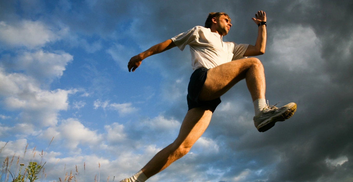 Man running outdoors against a backdrop of clouds, illustrating movement and physical activity related to movement analysis at New Approach Physical Therapy in Greenwood Village, CO.